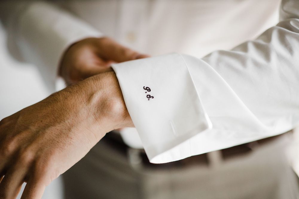 Close-up of hands adjusting a white dress shirt cuff with ace card detail.