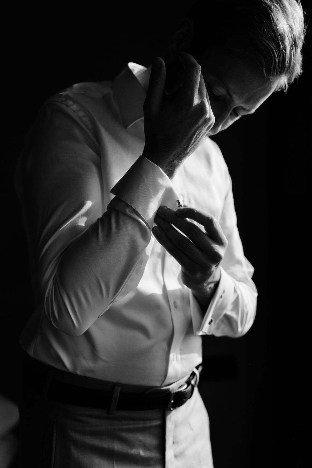 Dramatic black and white photo of a person in formal attire adjusting their collar.