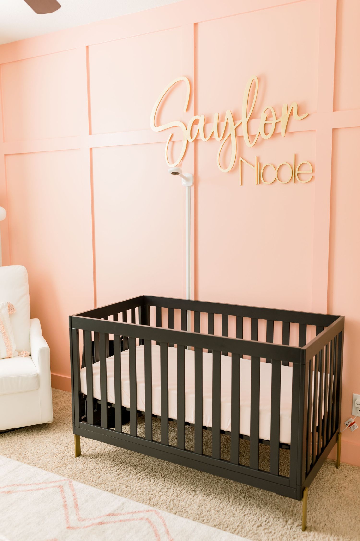 Elegant nursery featuring dark crib with gold accents against soft pink walls.