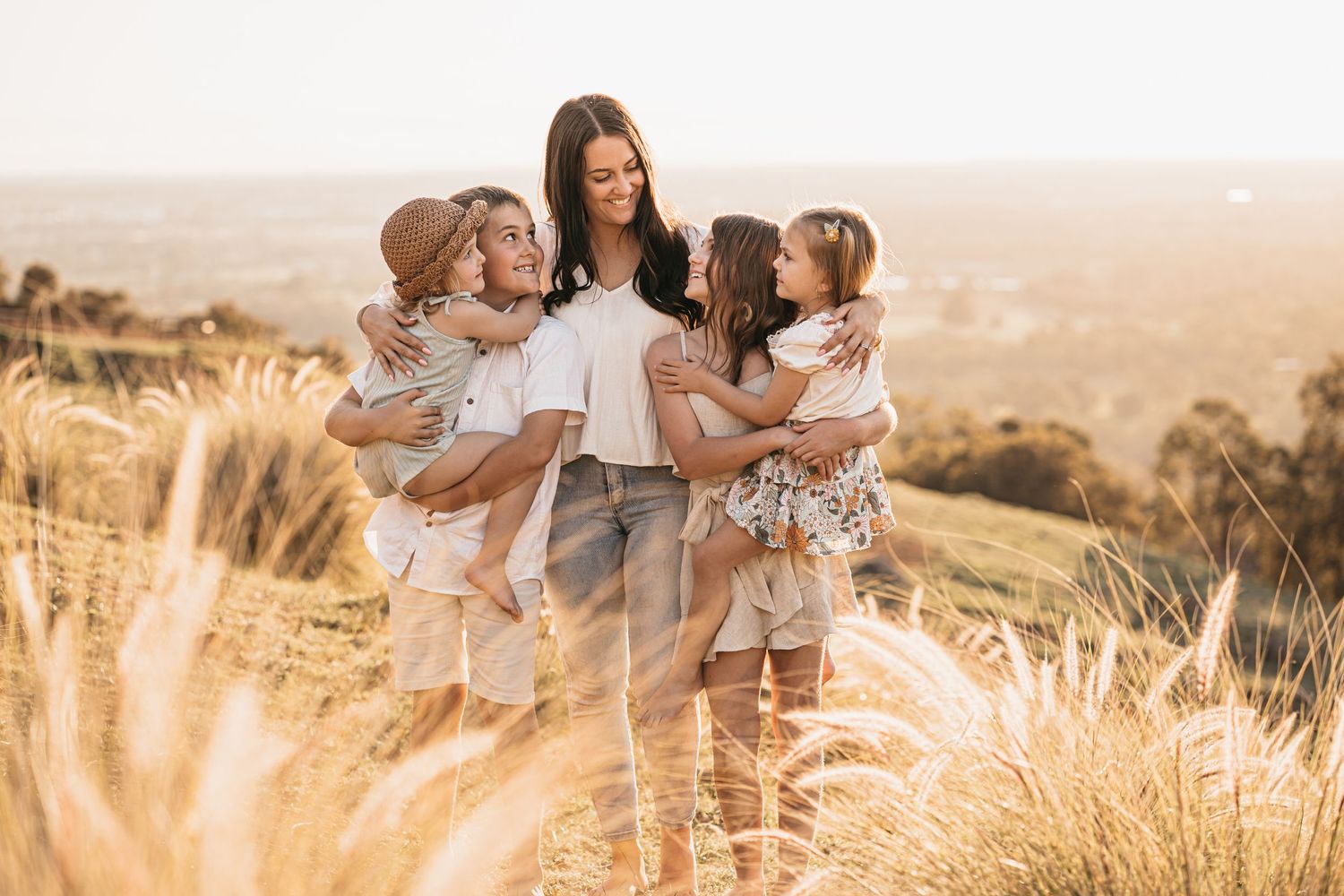 A tender family portrait in a sun-drenched field of golden grass at sunset.