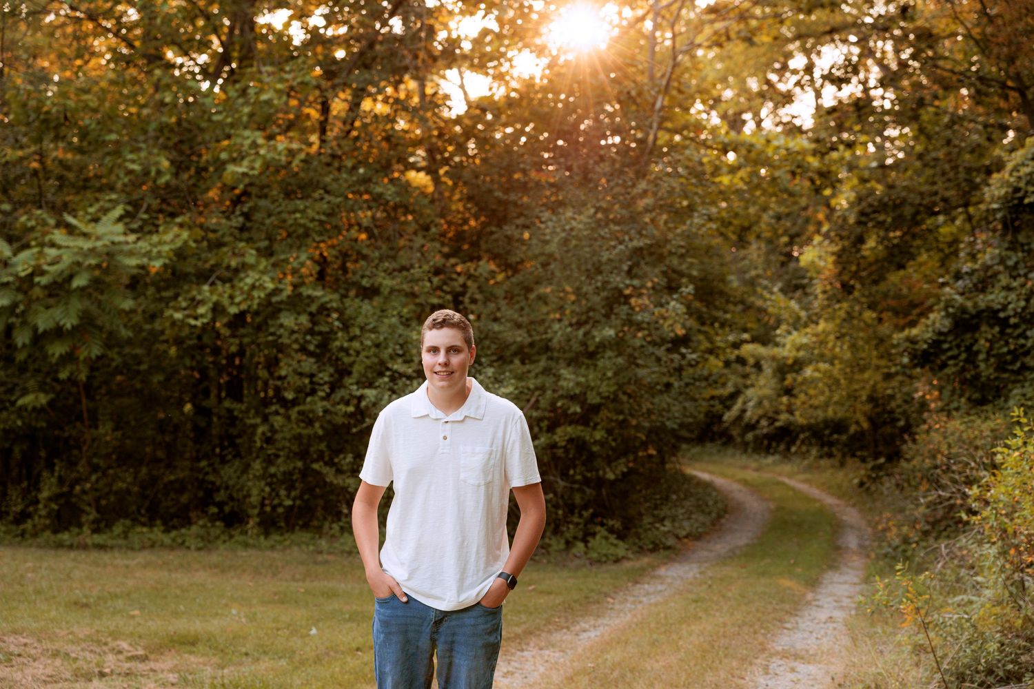 A sunset portrait on a winding dirt path with golden sunlight filtering through trees.