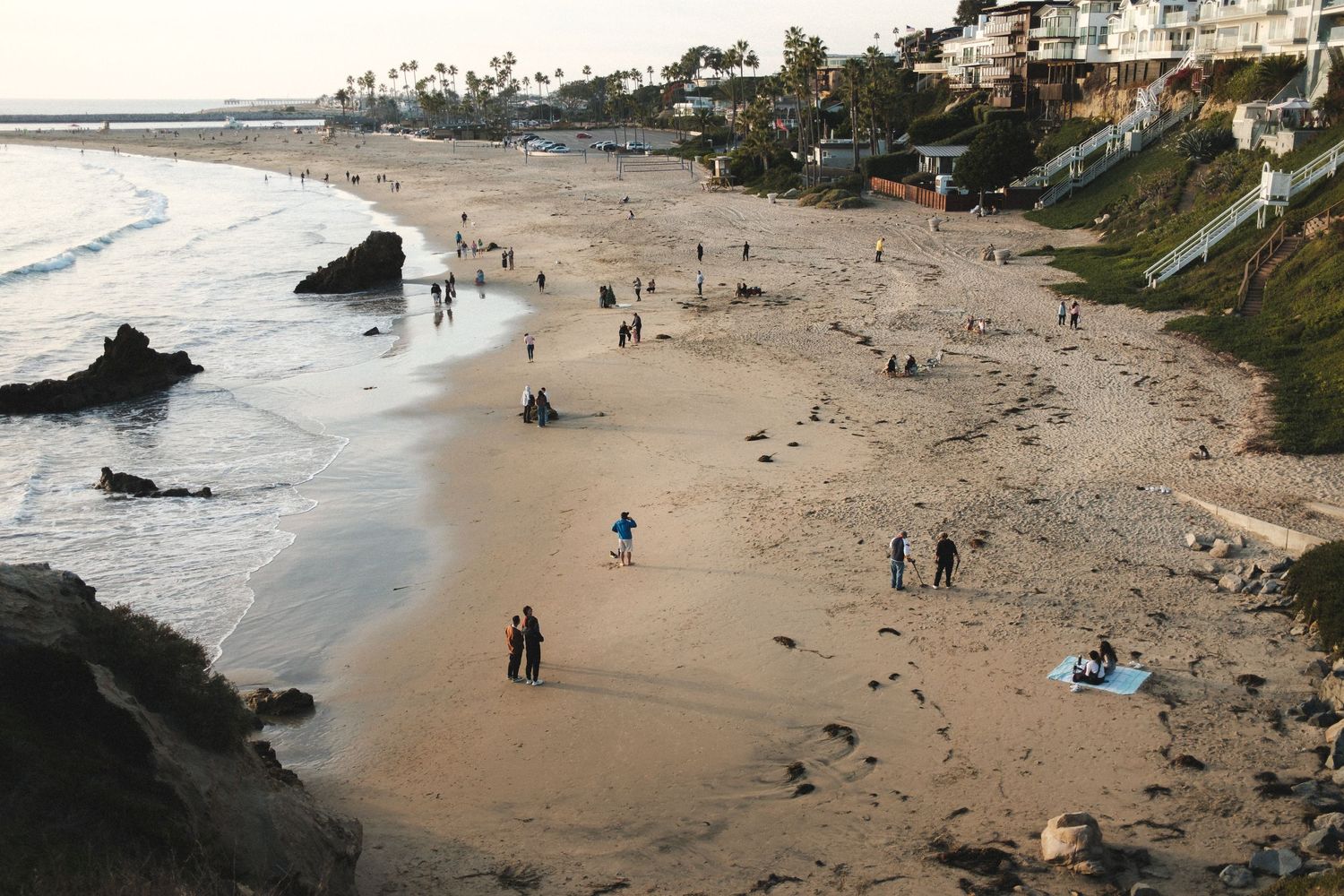 Aerial view of a scenic beach with palm trees and beachgoers on a cloudy day.