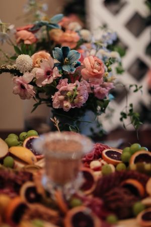 A colorful arrangement of peach roses and blue flowers next to a fruit platter.