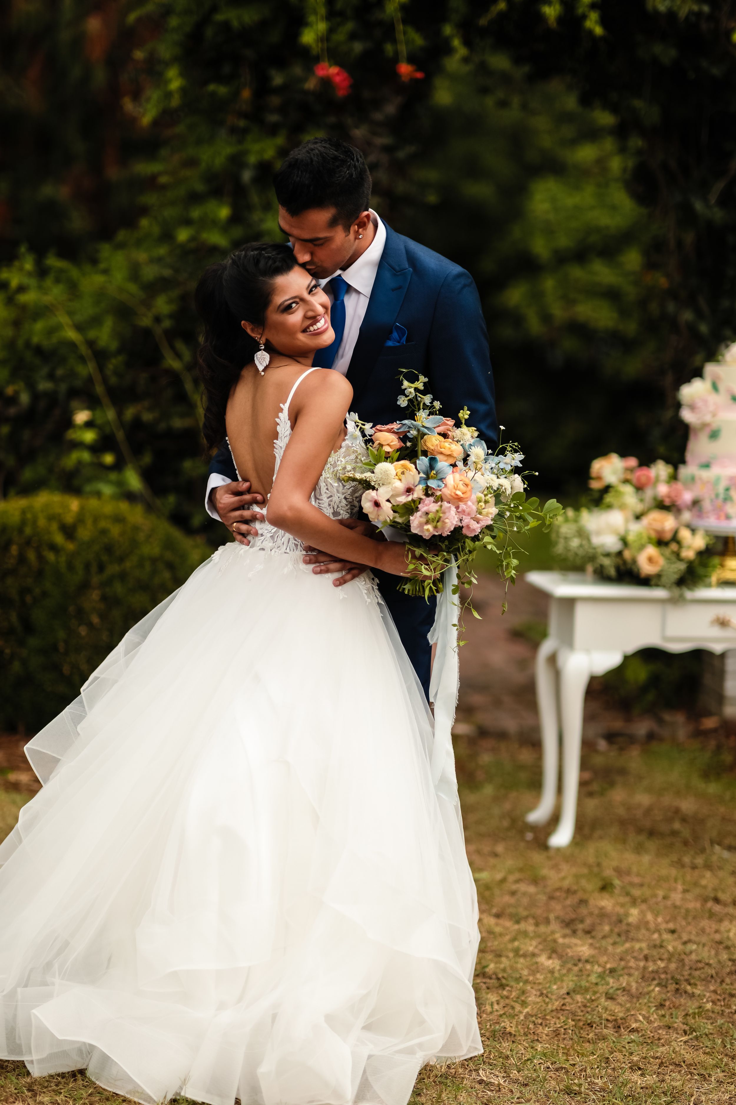 A romantic wedding moment captured as the couple embraces in a garden setting with a decorative table.