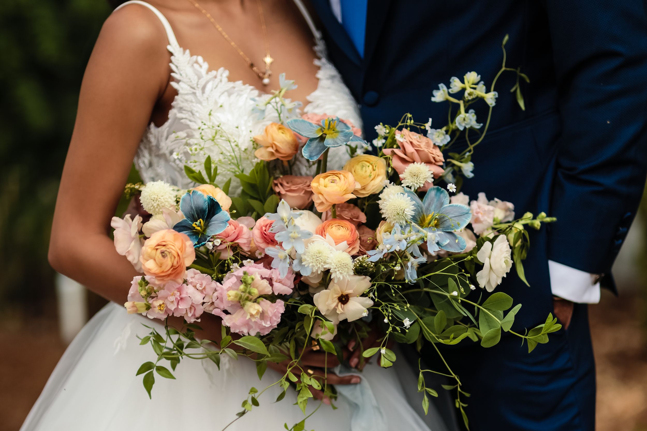 Close-up of a stunning bridal bouquet featuring peach roses, blue flowers, and delicate greenery.