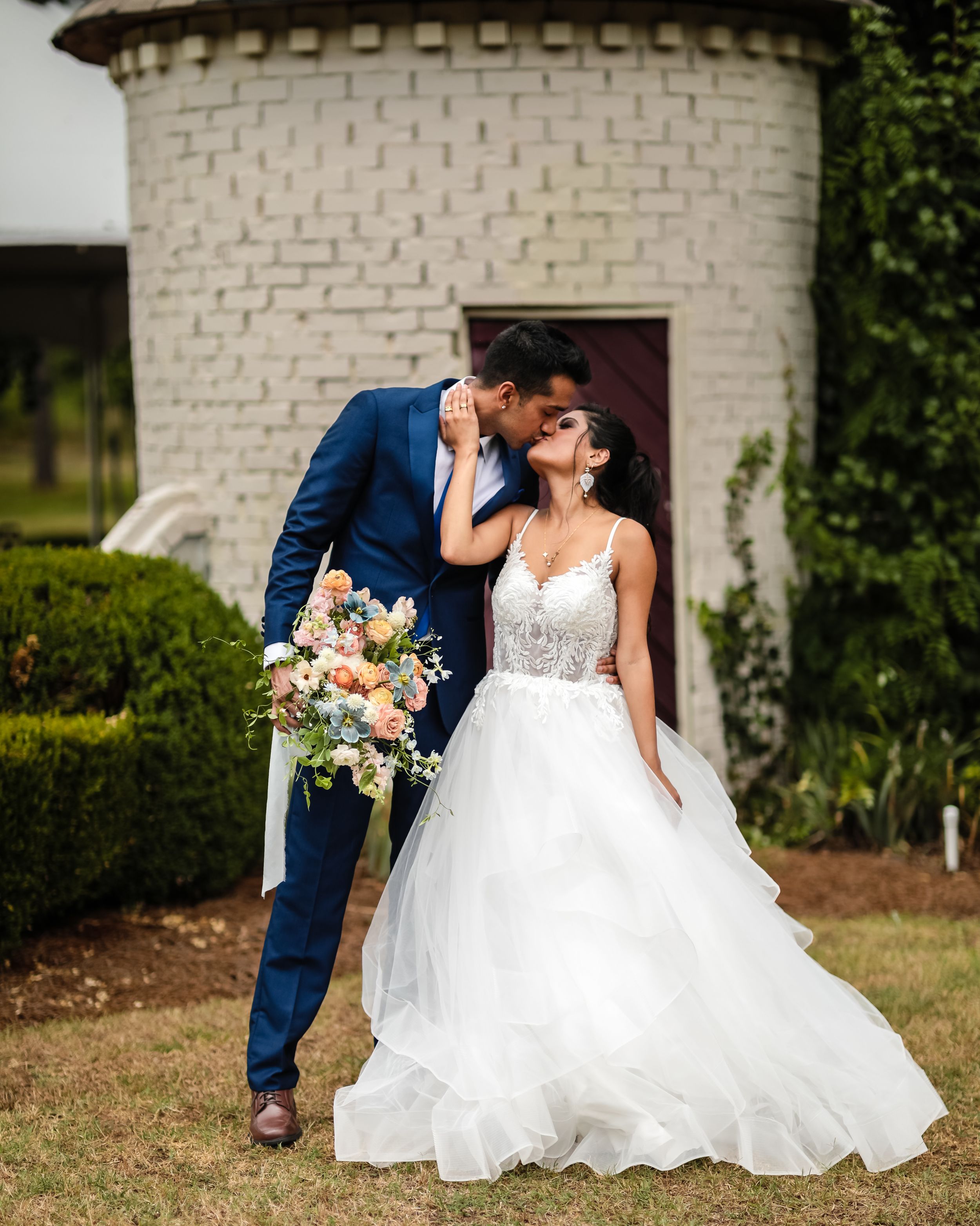 A romantic wedding portrait in front of a white brick structure with a flowing bridal gown.