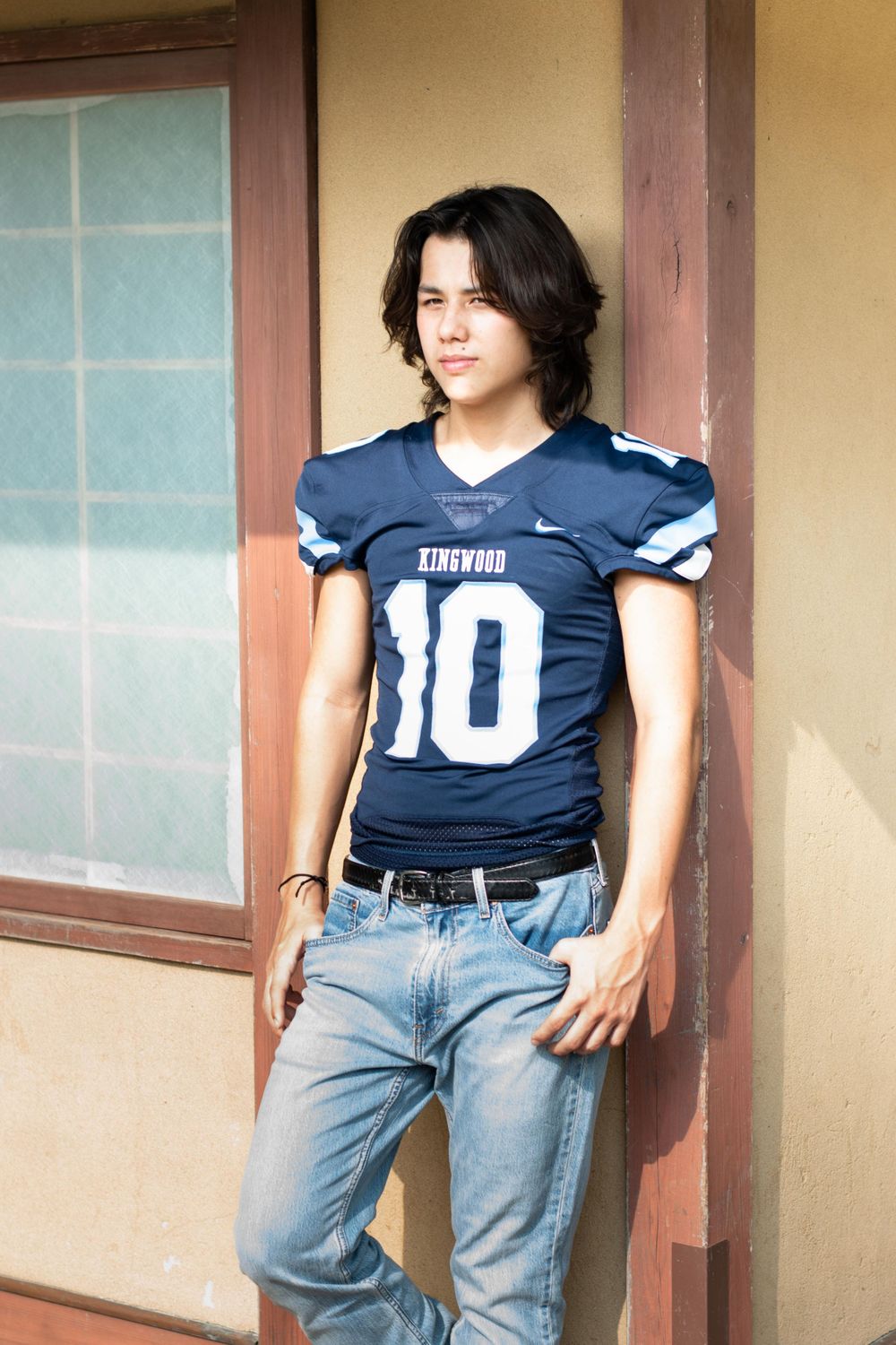 Athletic figure in navy football jersey number 10 posing against traditional building exterior.