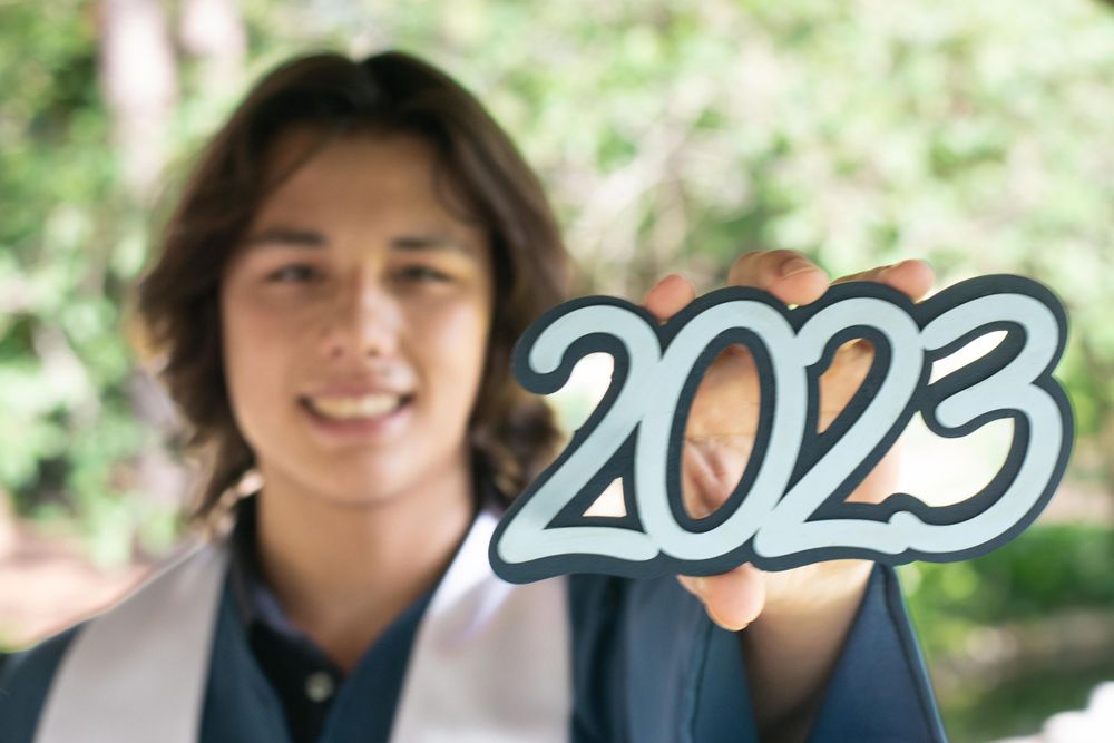 Graduate holding up '2023' numbers in graduation attire outdoors.