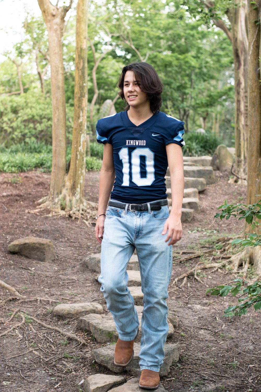 Someone wearing a blue football jersey numbered 10 and jeans walking along a wooded trail.