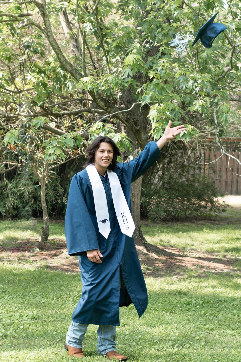 Graduate in blue cap and gown throwing graduation cap in celebration outdoors.