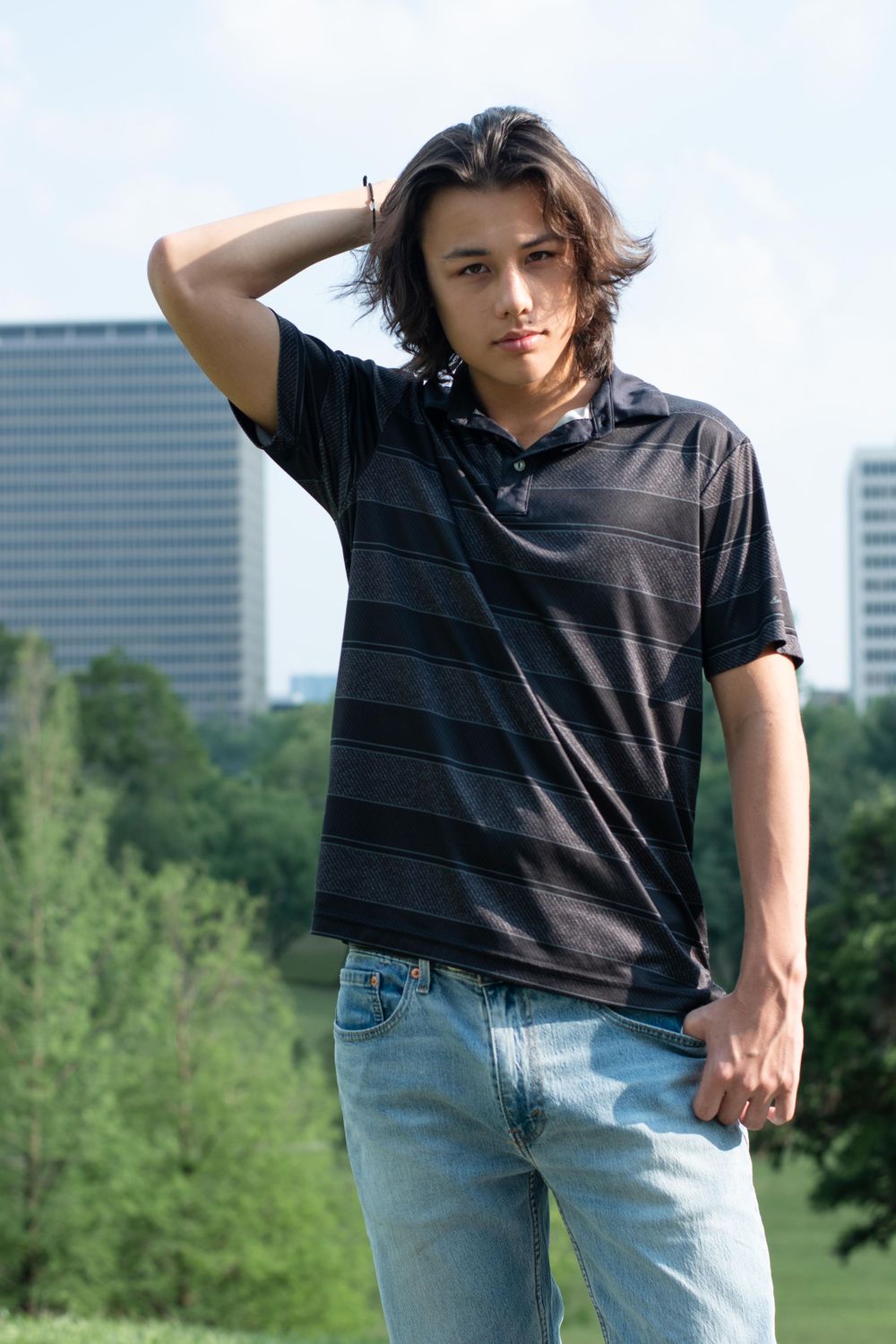 Casual outdoor portrait against city skyline wearing striped polo shirt and jeans.