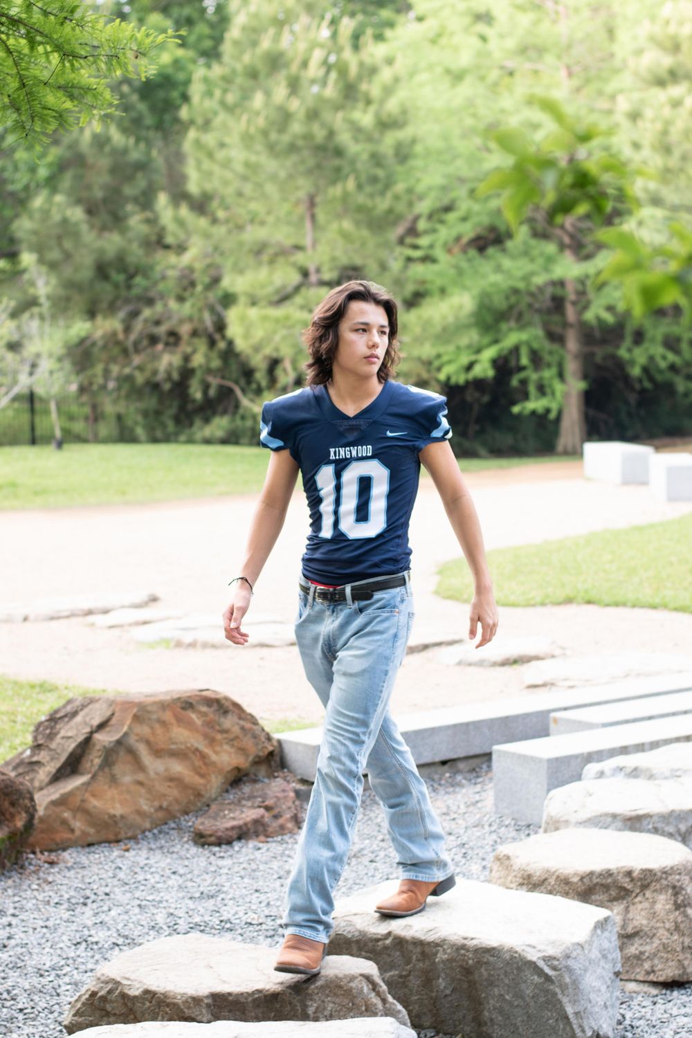 Athletic figure in blue jersey number 10 walking along stone path in natural setting.