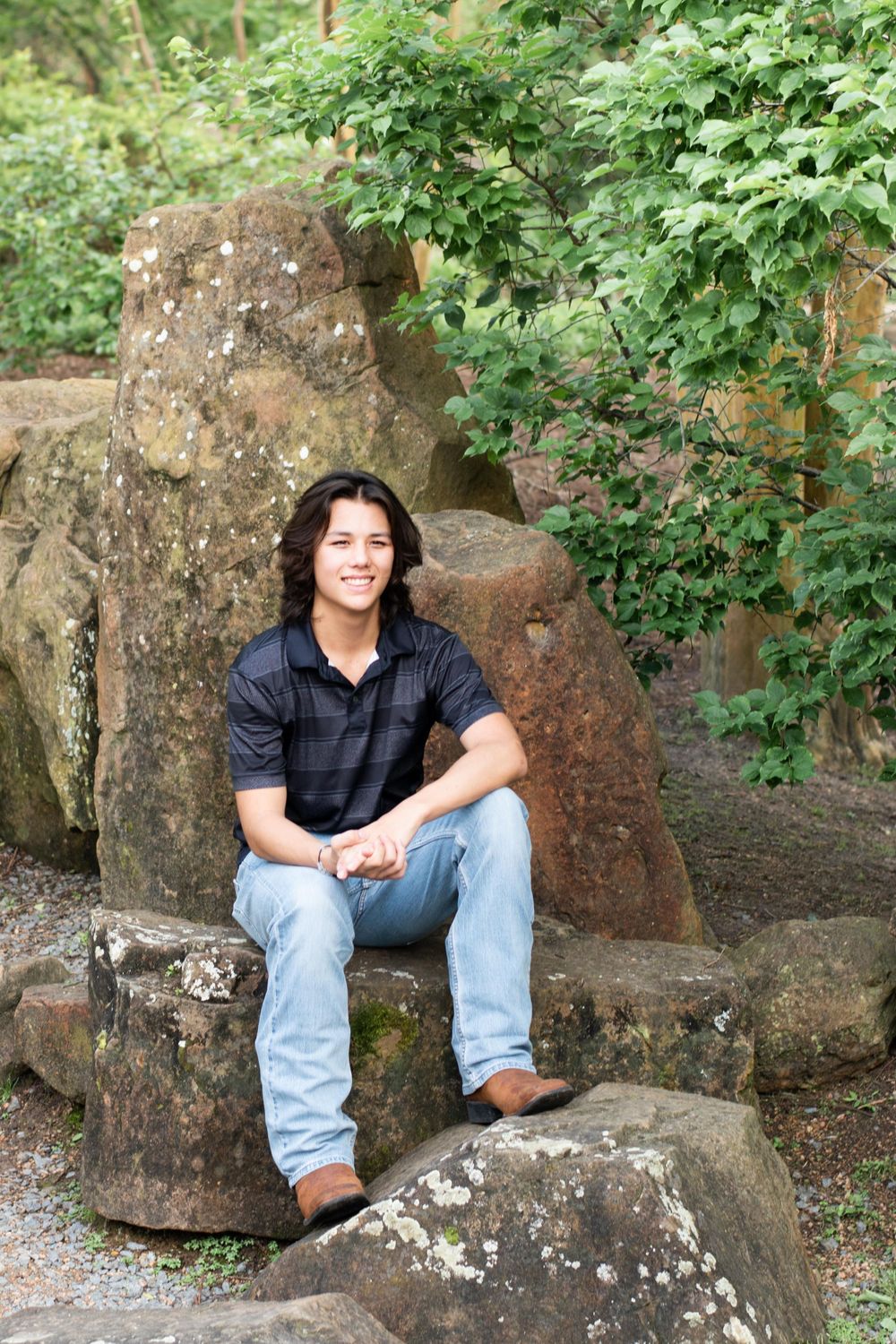Relaxed outdoor portrait on mossy rocks surrounded by green foliage.