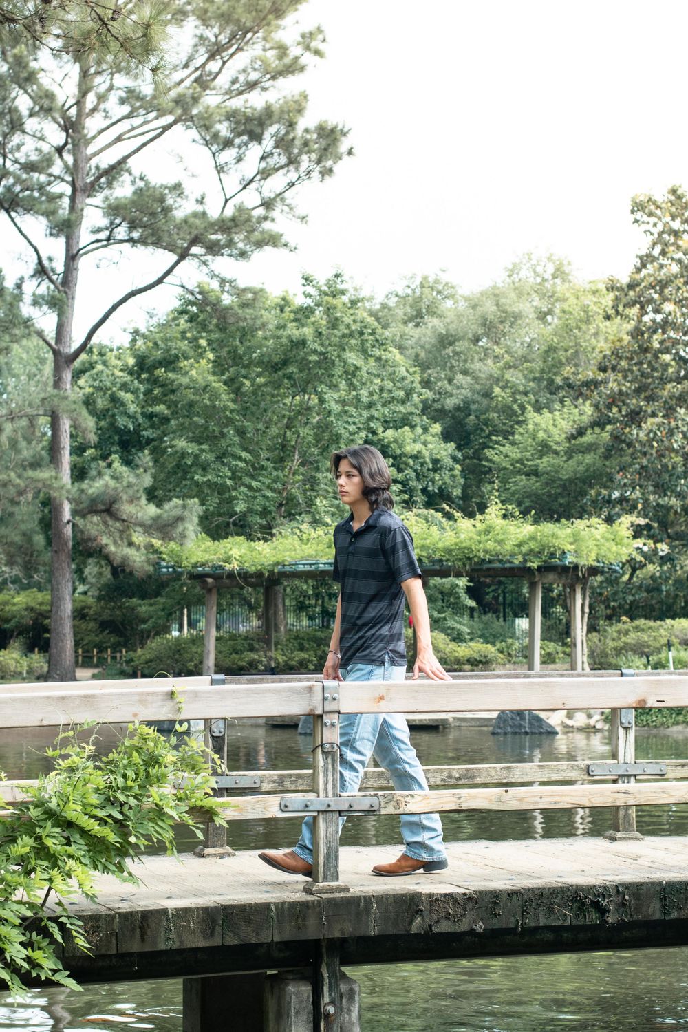 A person walking across a wooden dock over water in a natural park setting wearing casual attire.