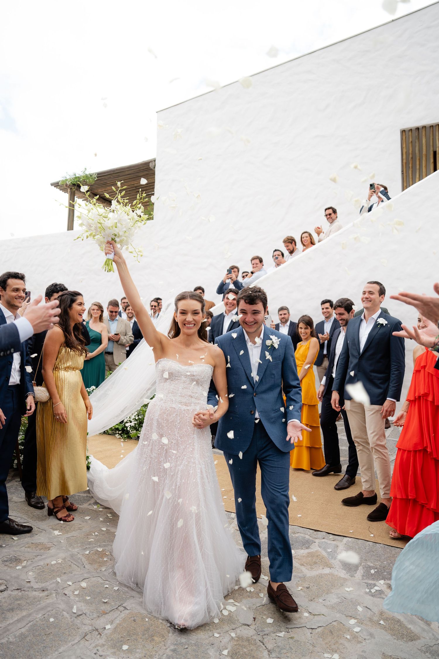 Newlyweds celebrate with guests throwing confetti during an outdoor wedding reception.