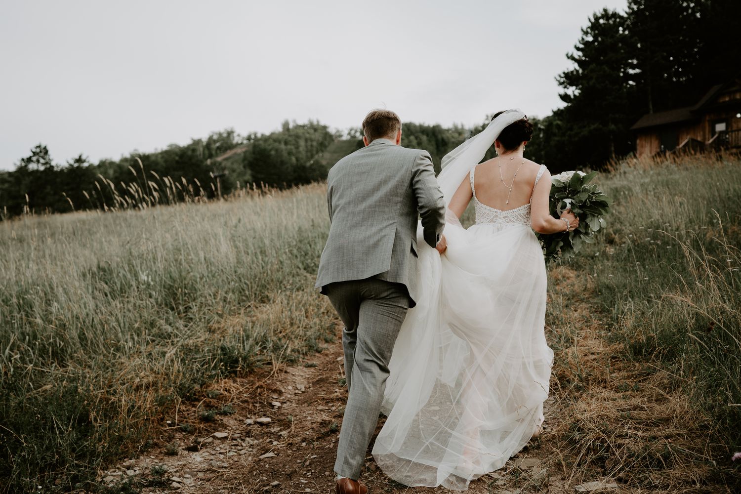 groom holding brides train as they climb uphill