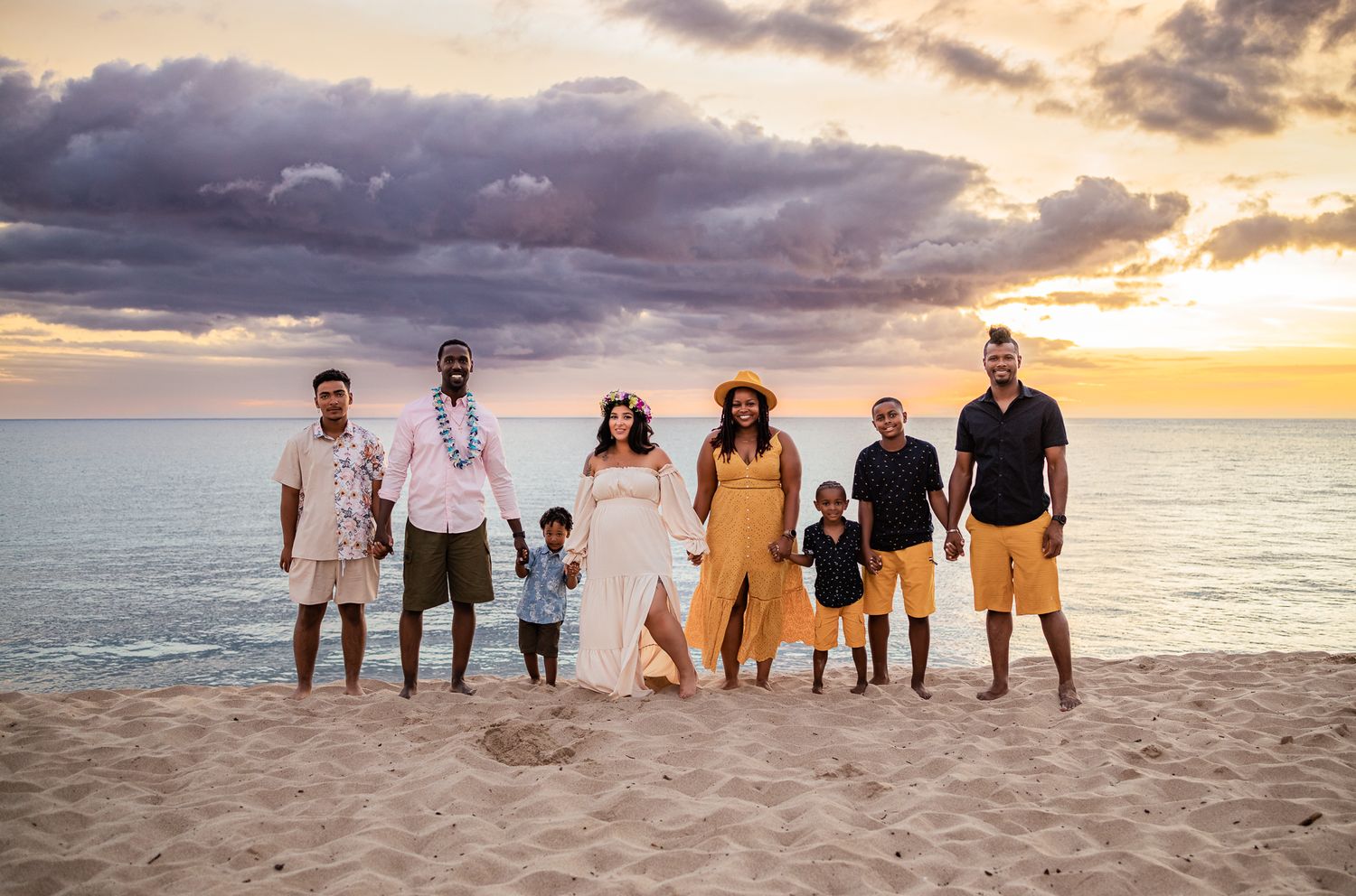 Group portrait of family members standing together on beach at sunset.