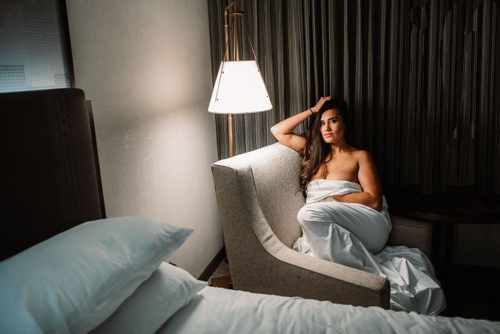 Intimate bedroom portrait with soft hotel lighting and white bedding.