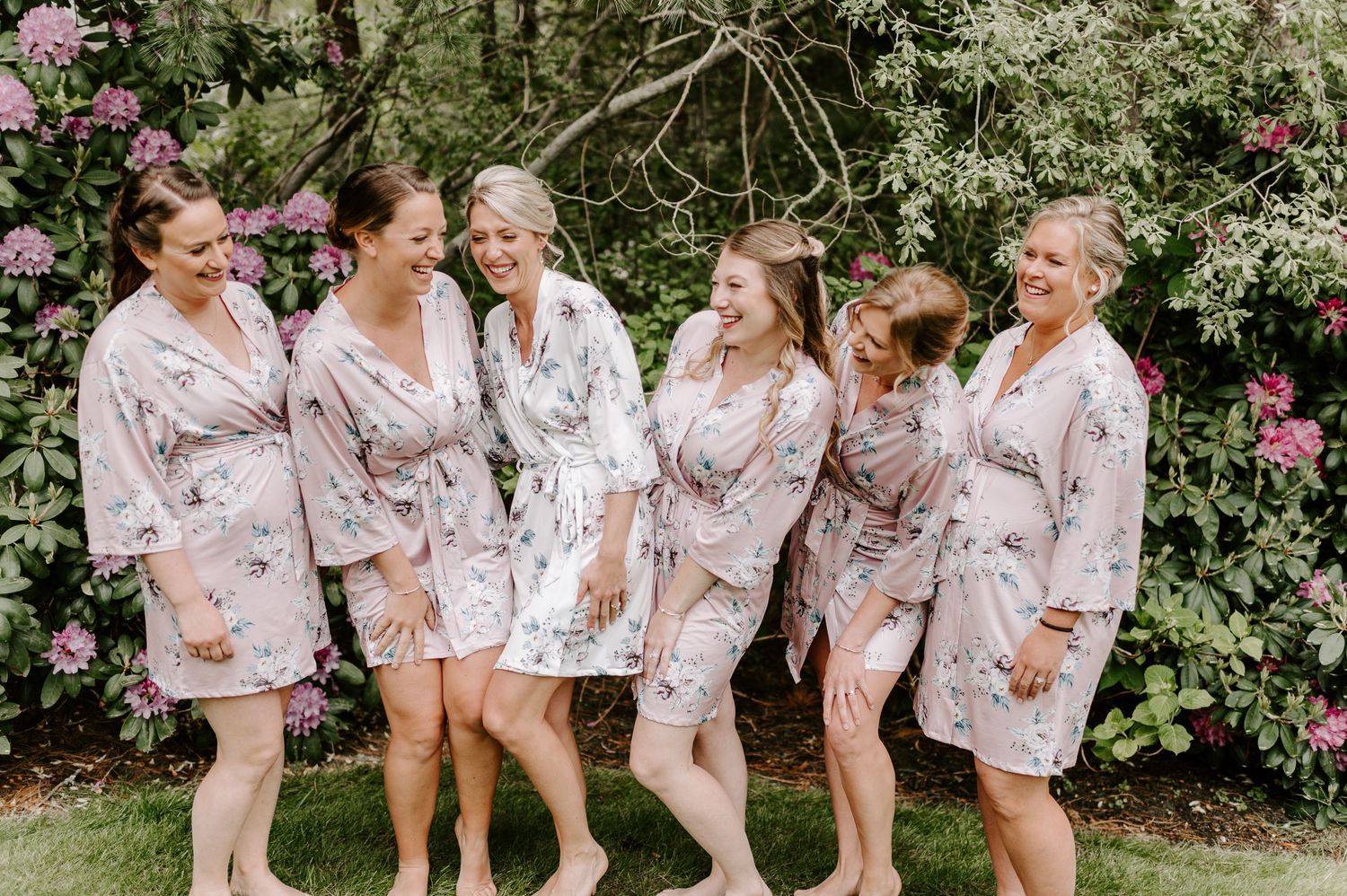 Bridesmaids in matching floral robes pose together in a garden setting.