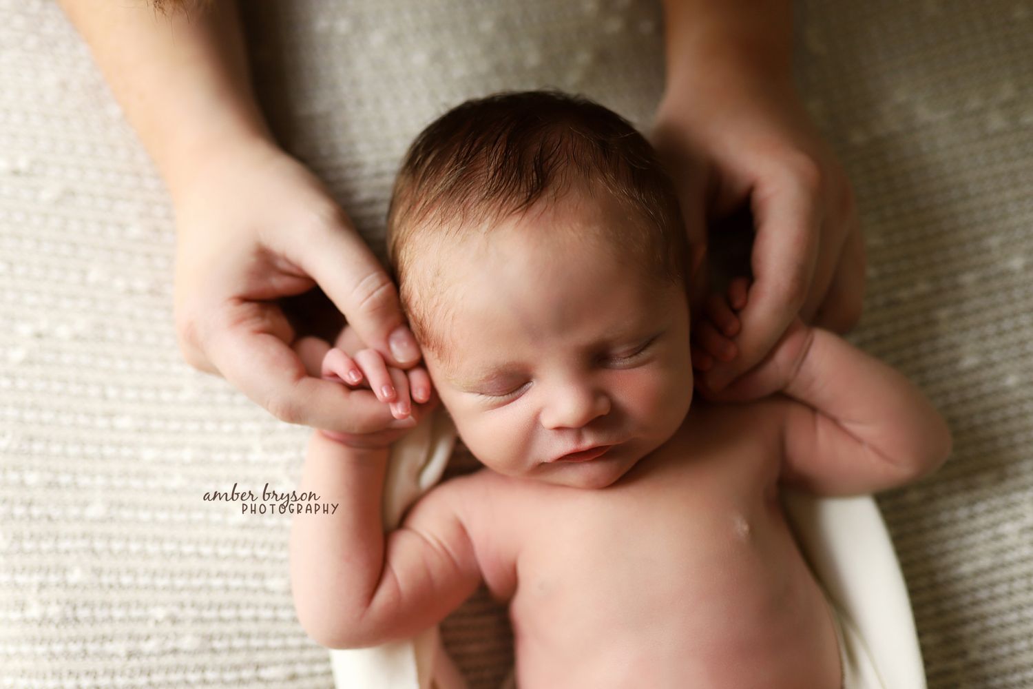 Gentle hands supporting sleeping newborn during photoshoot on white background.