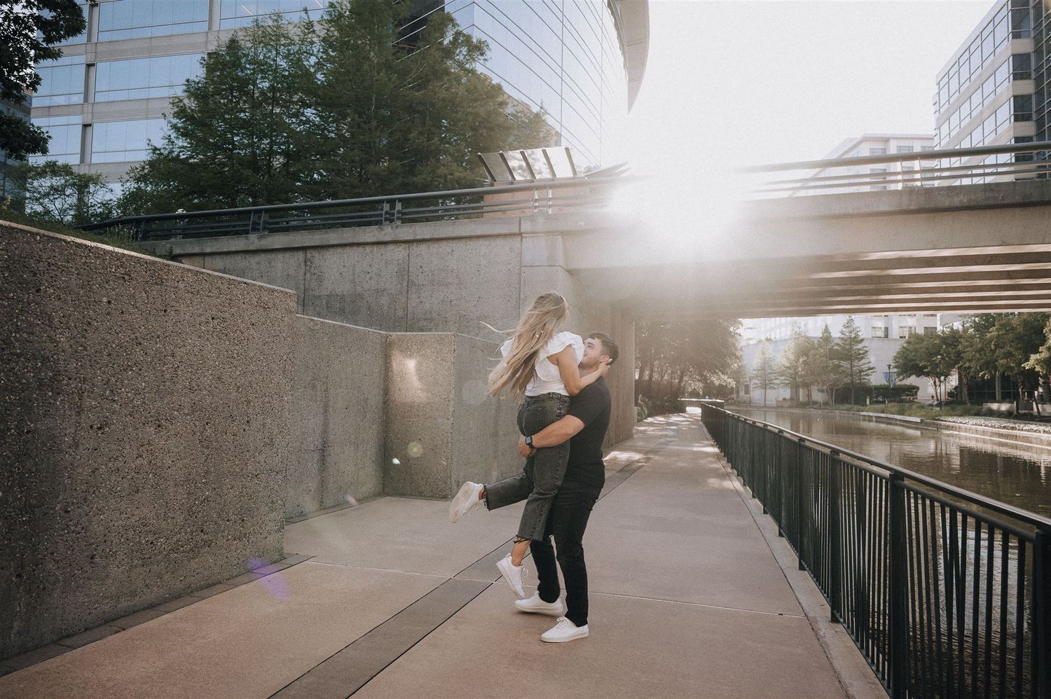 A silhouetted couple sharing an intimate moment on a riverside path at dusk.