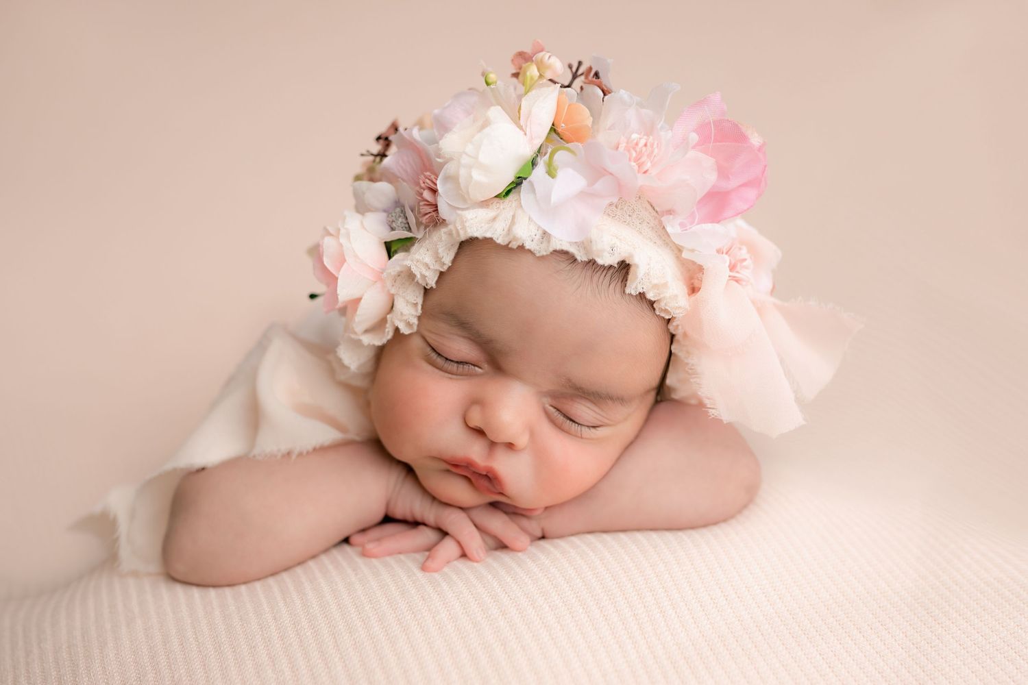 Sleeping newborn wearing delicate floral crown with pink and white flowers rests peacefully on soft fabric.