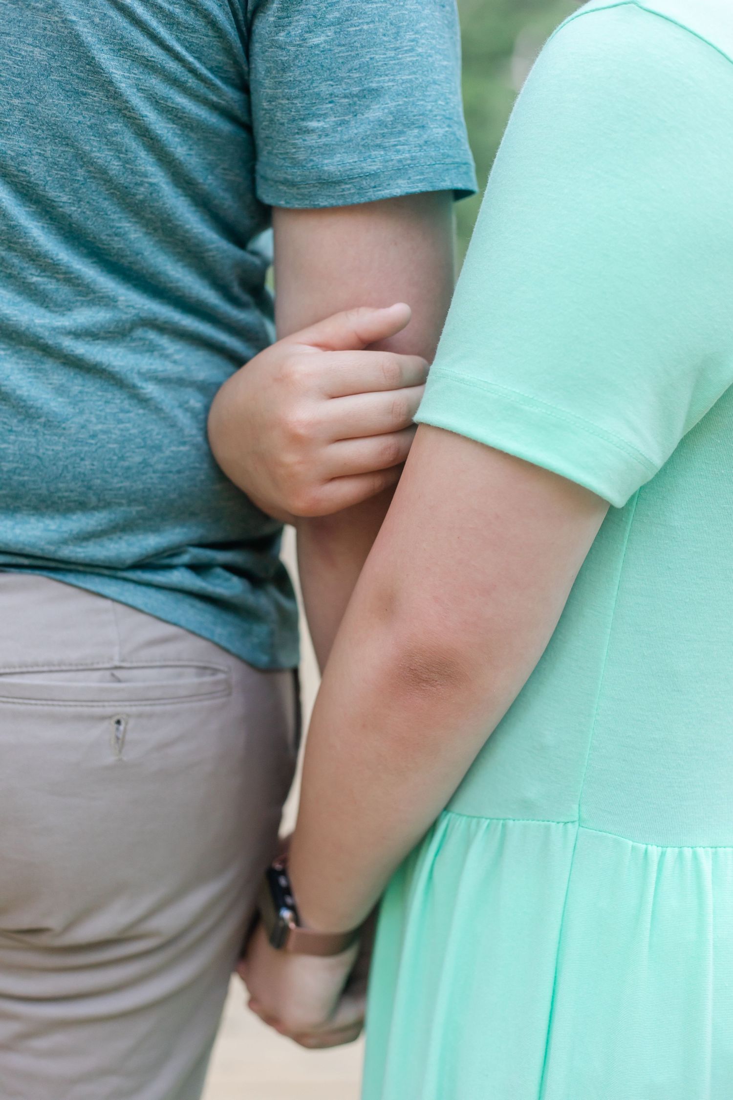 Close-up detail of mint green dress fabric and gray clothing as two people stand close together.