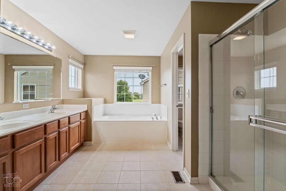 Spacious master bathroom featuring double vanity, soaking tub, and glass shower enclosure with beige tile flooring.