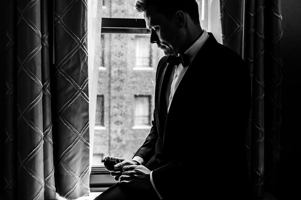 A dramatic silhouette of a groom adjusting his cuffs by a window.