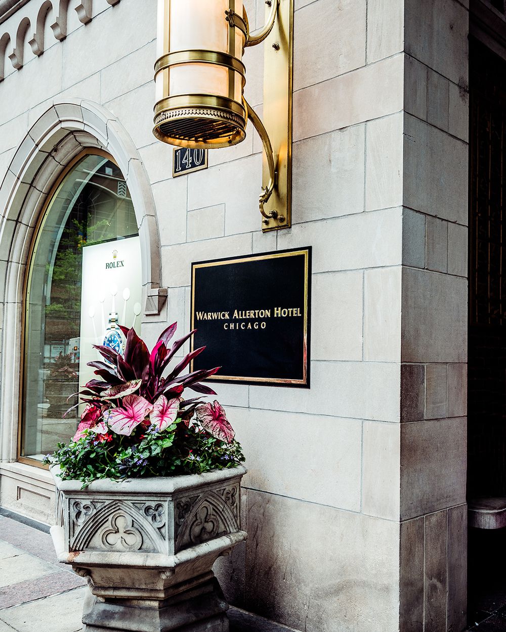 Ornate hotel entrance with brass lamp and decorative floral planter at the Warwick Allerton Hotel.