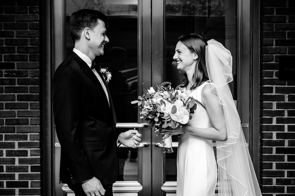 A black and white wedding portrait of a couple sharing a joyful moment with bridal bouquet.