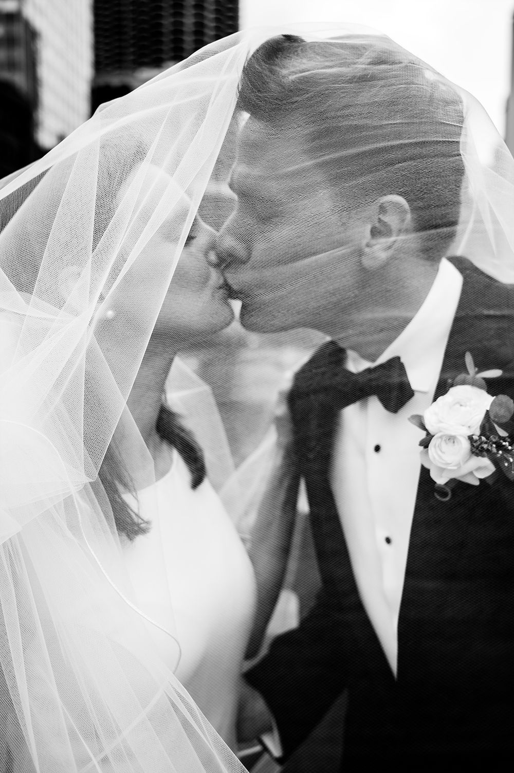 Intimate black and white wedding portrait under flowing veil with delicate bouquet.