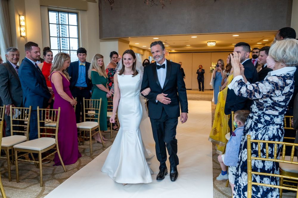 Wedding ceremony exit with guests celebrating in elegant indoor venue with gold chairs.