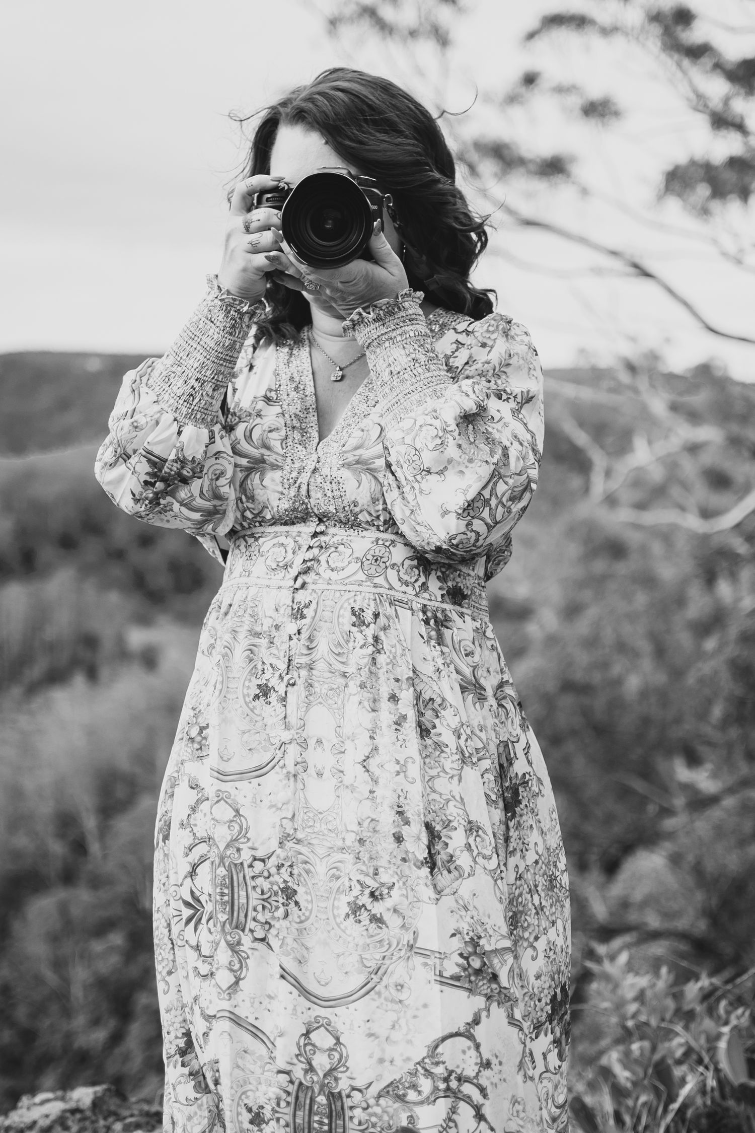 Photographer in floral dress taking picture with professional camera in outdoor setting.