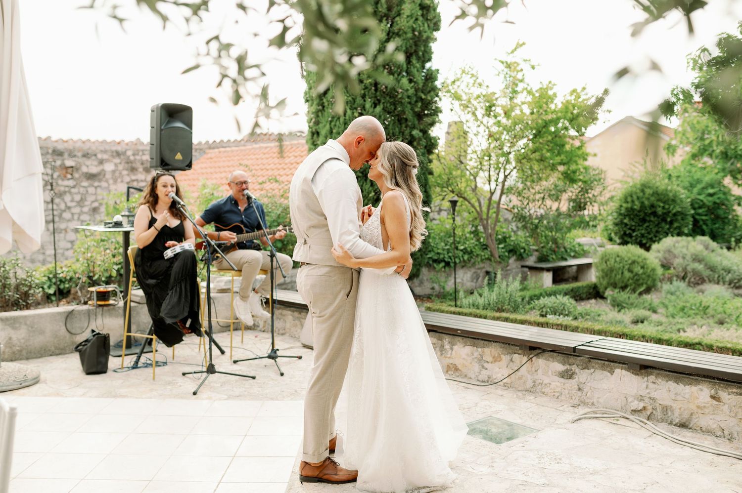 Outdoor garden wedding ceremony with musicians performing in background.