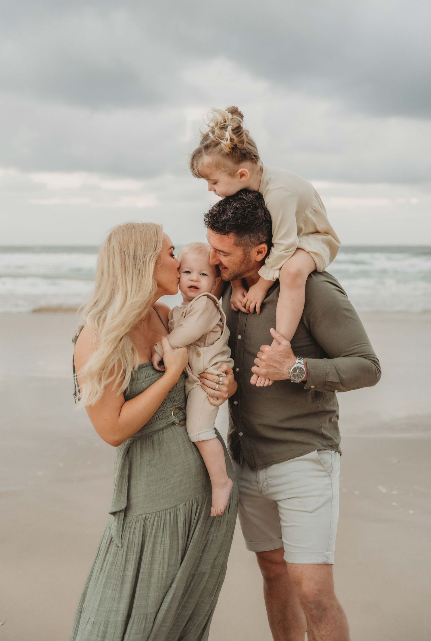 Siblings giggling on the beach with their mum and dad watching the sunset