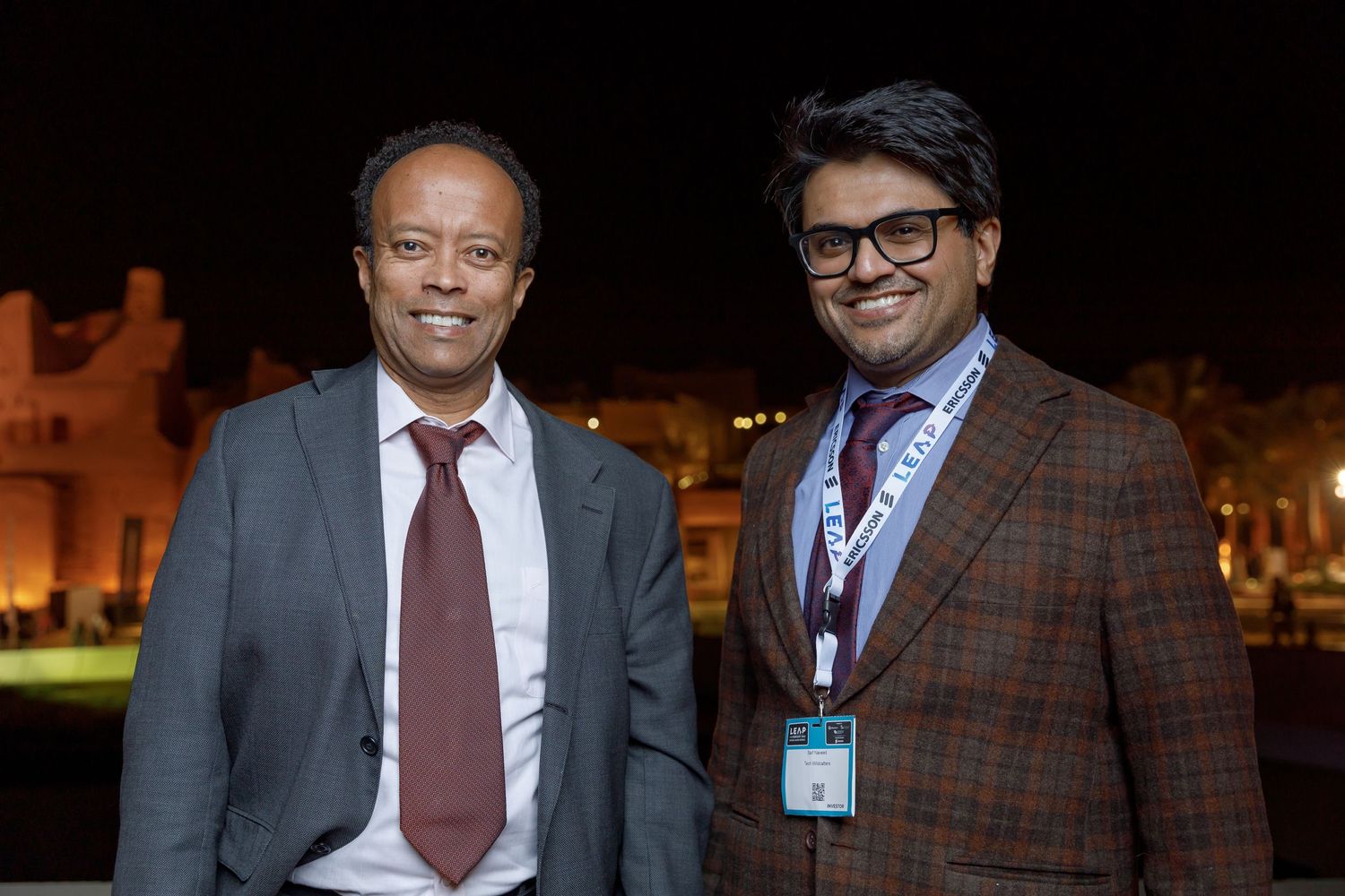 Two people in formal business attire standing together at night outdoors.