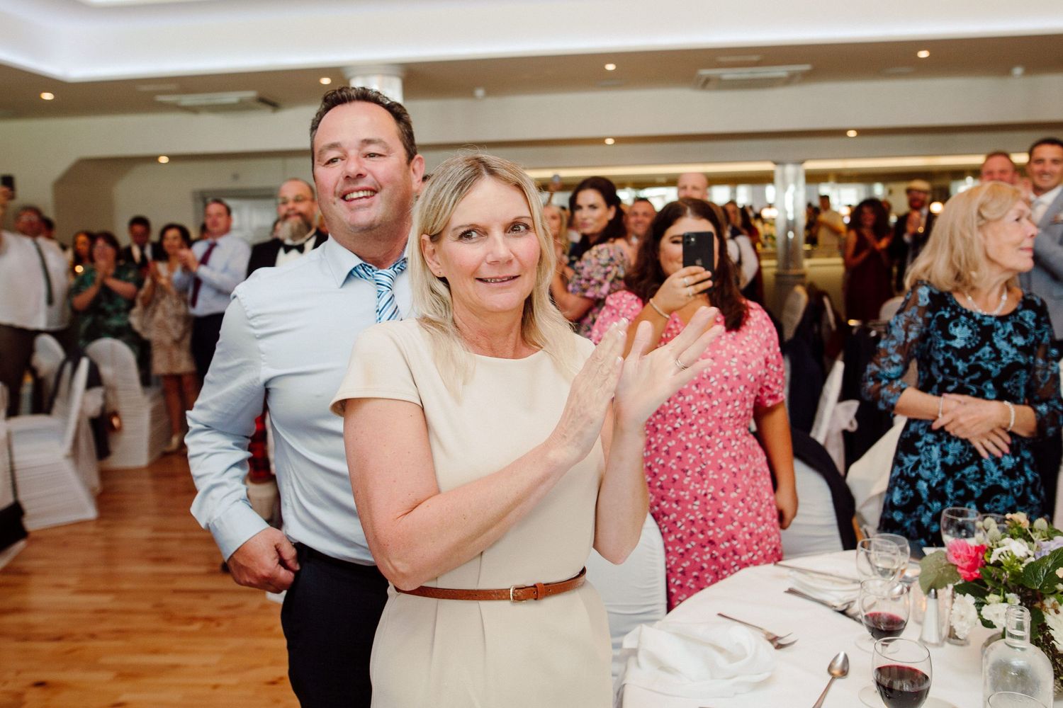Wedding guests clapping and enjoying festivities at an indoor reception.