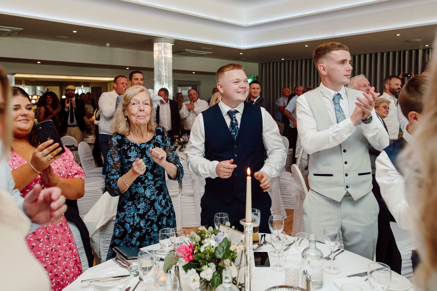 Wedding guests standing and applauding during a reception celebration.