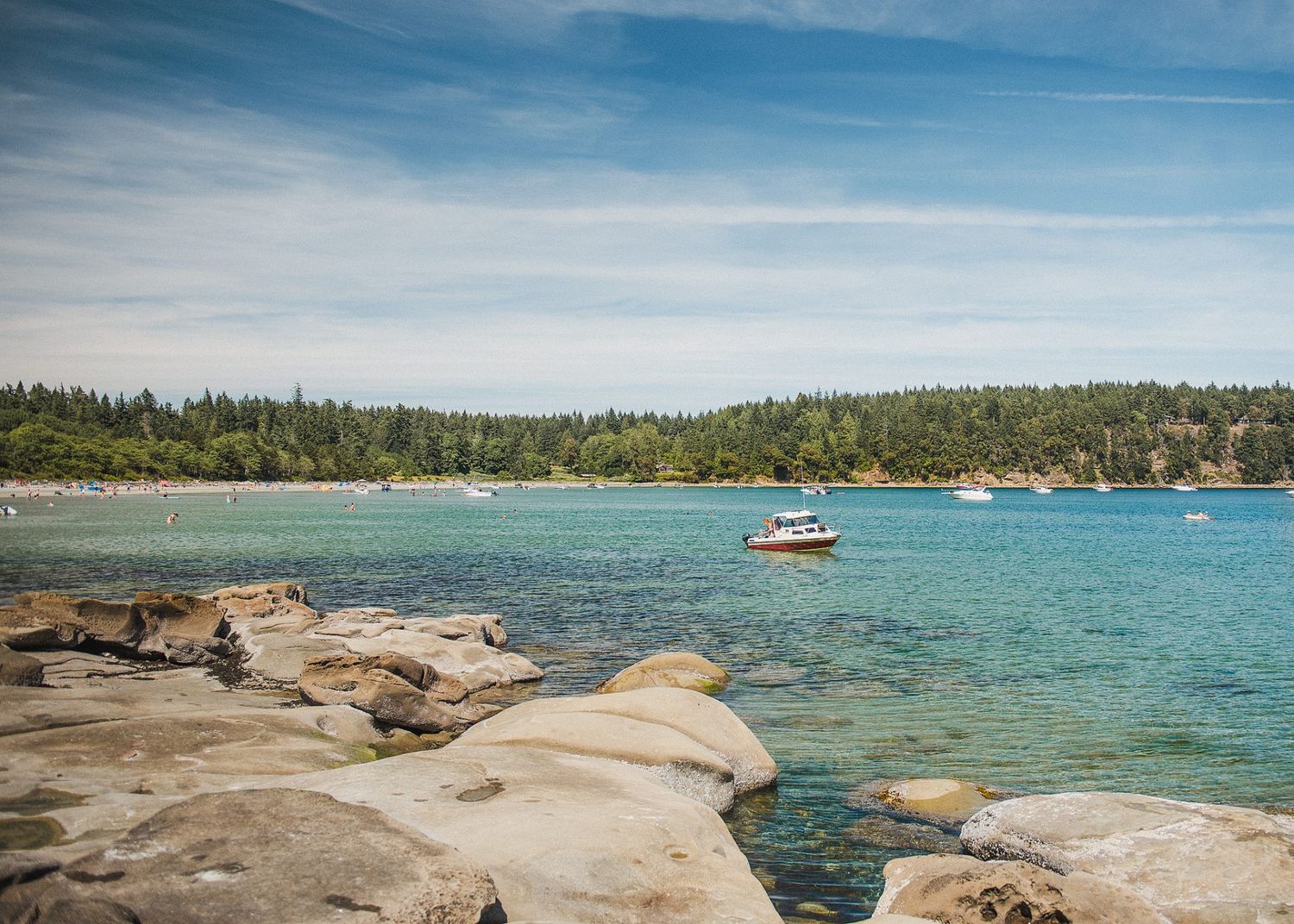 Smooth rock formations line turquoise bay with boats and forested shore in background.