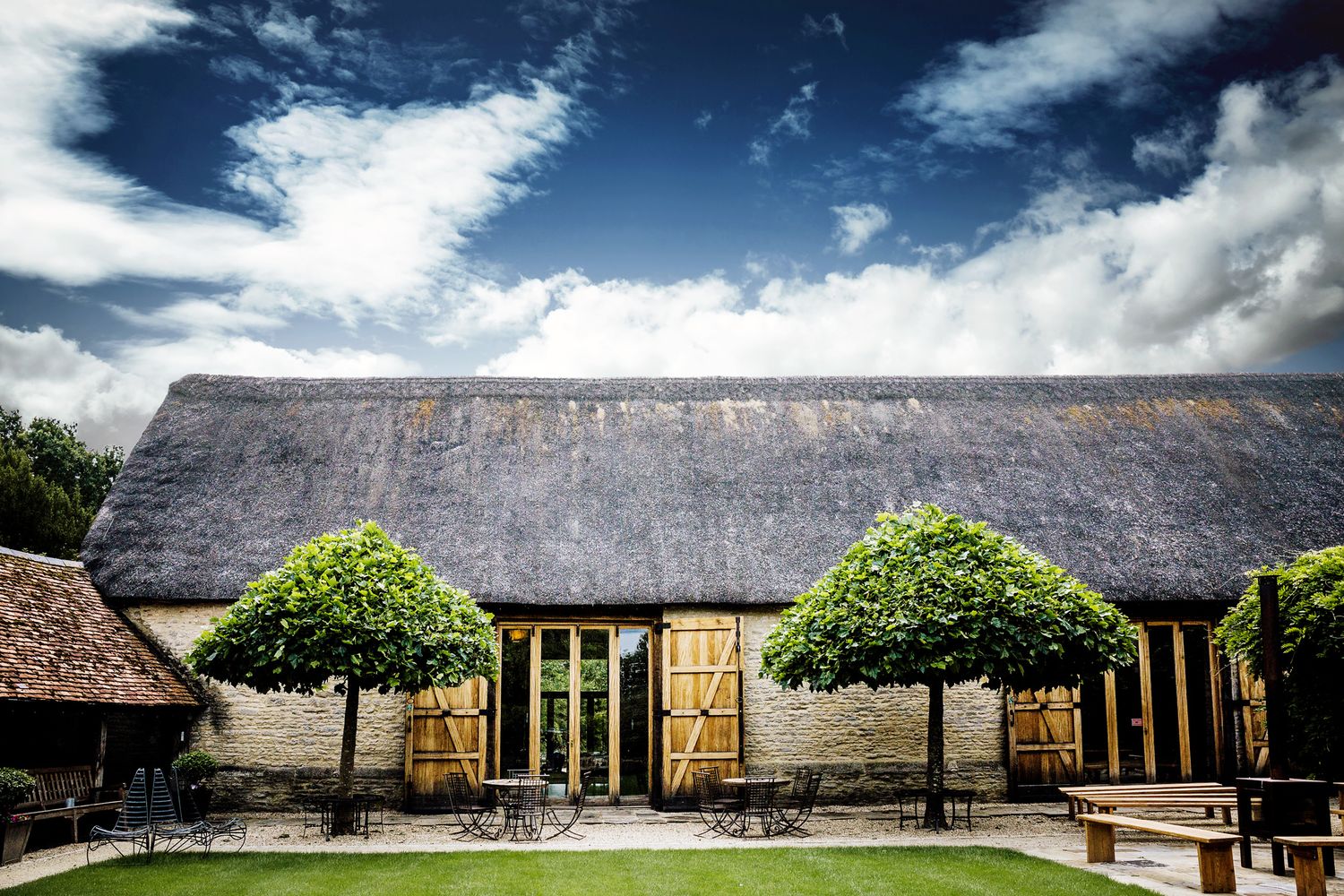 Traditional thatched-roof barn venue with symmetrical topiary trees framing the entrance.