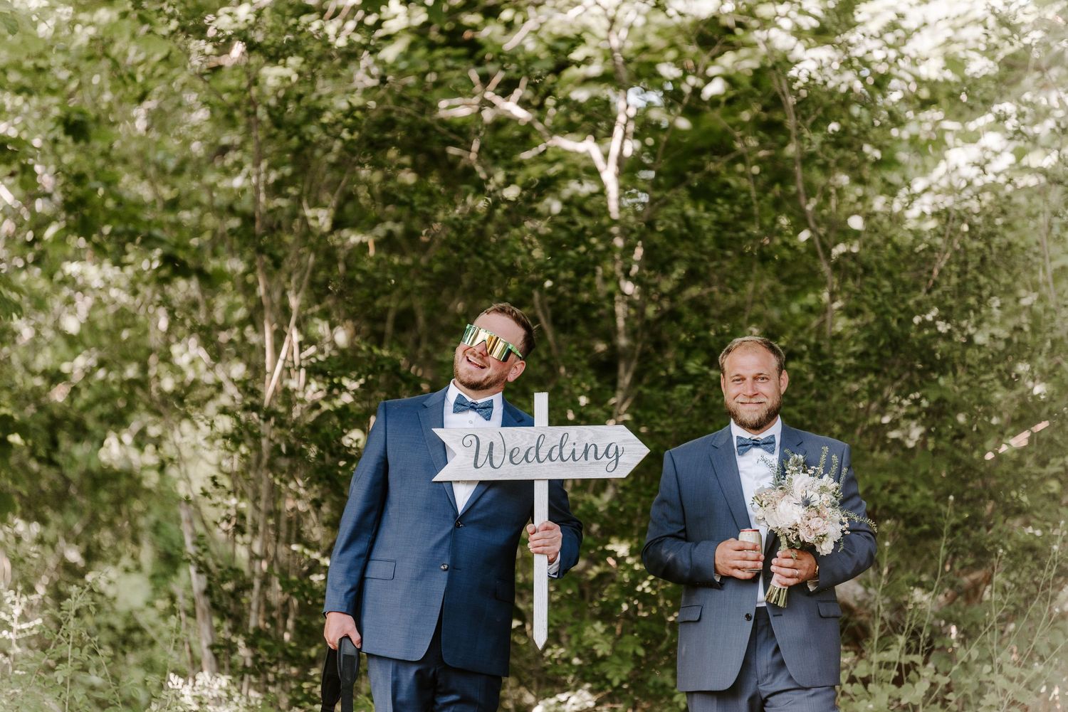 Two people in blue suits share a candid moment outdoors during a wedding celebration.