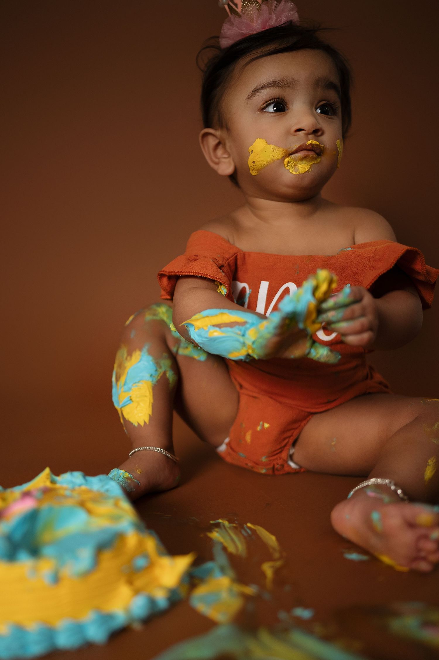 Baby wearing crown gets messy with colorful cake during cake smash photo session.