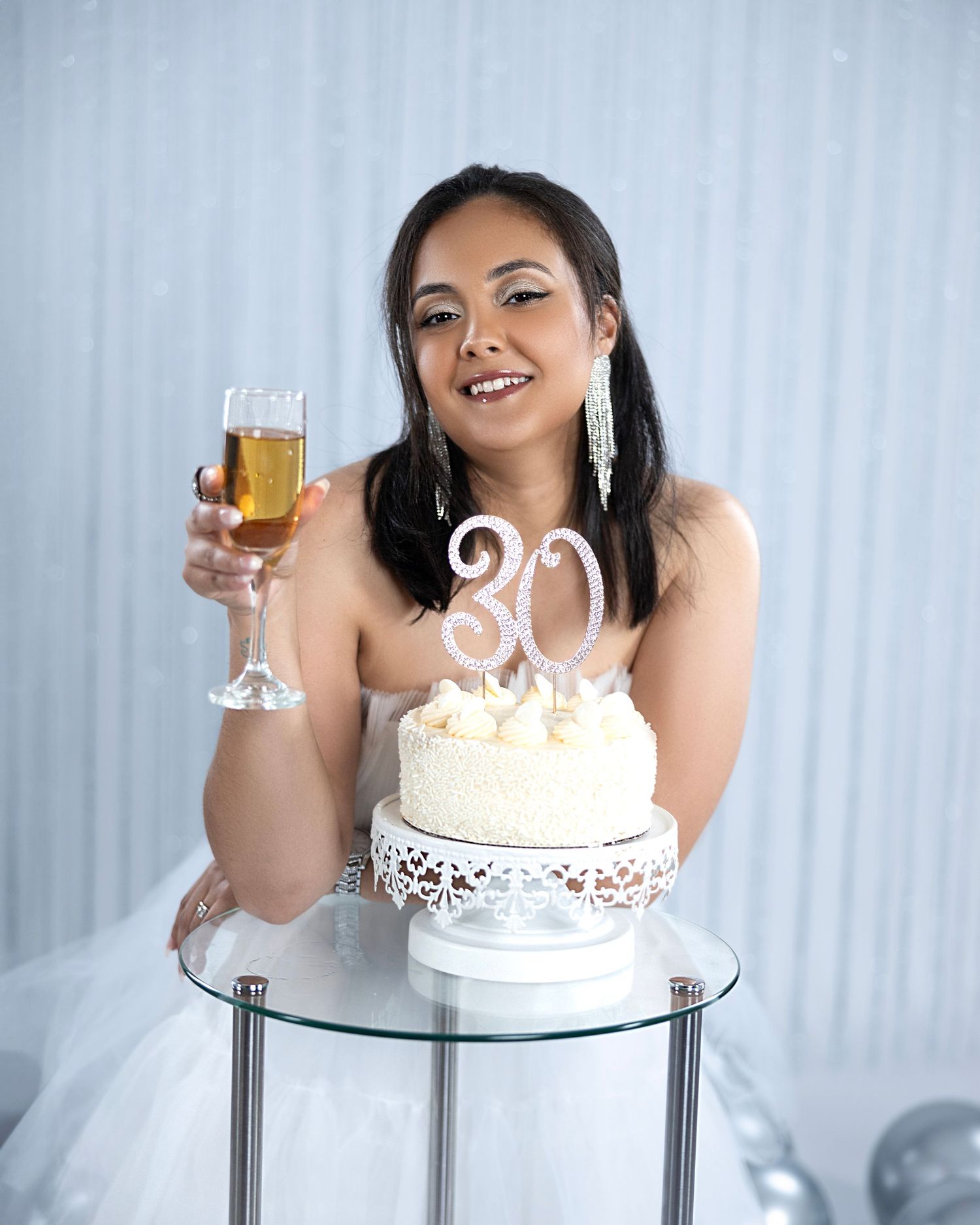 Birthday celebration photo with white cake and champagne glass on glass table.