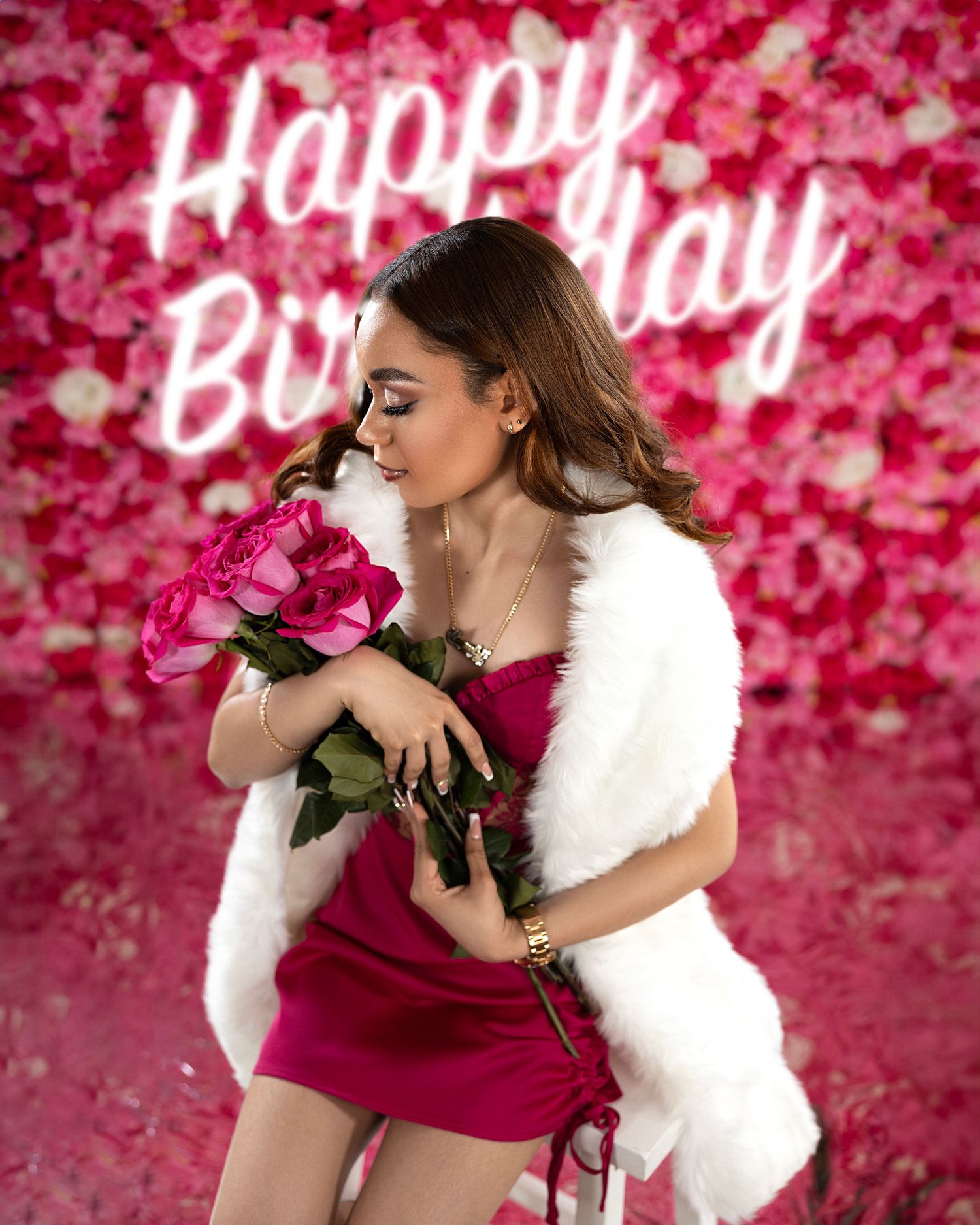 Birthday photoshoot with roses in front of pink neon sign and floral backdrop.