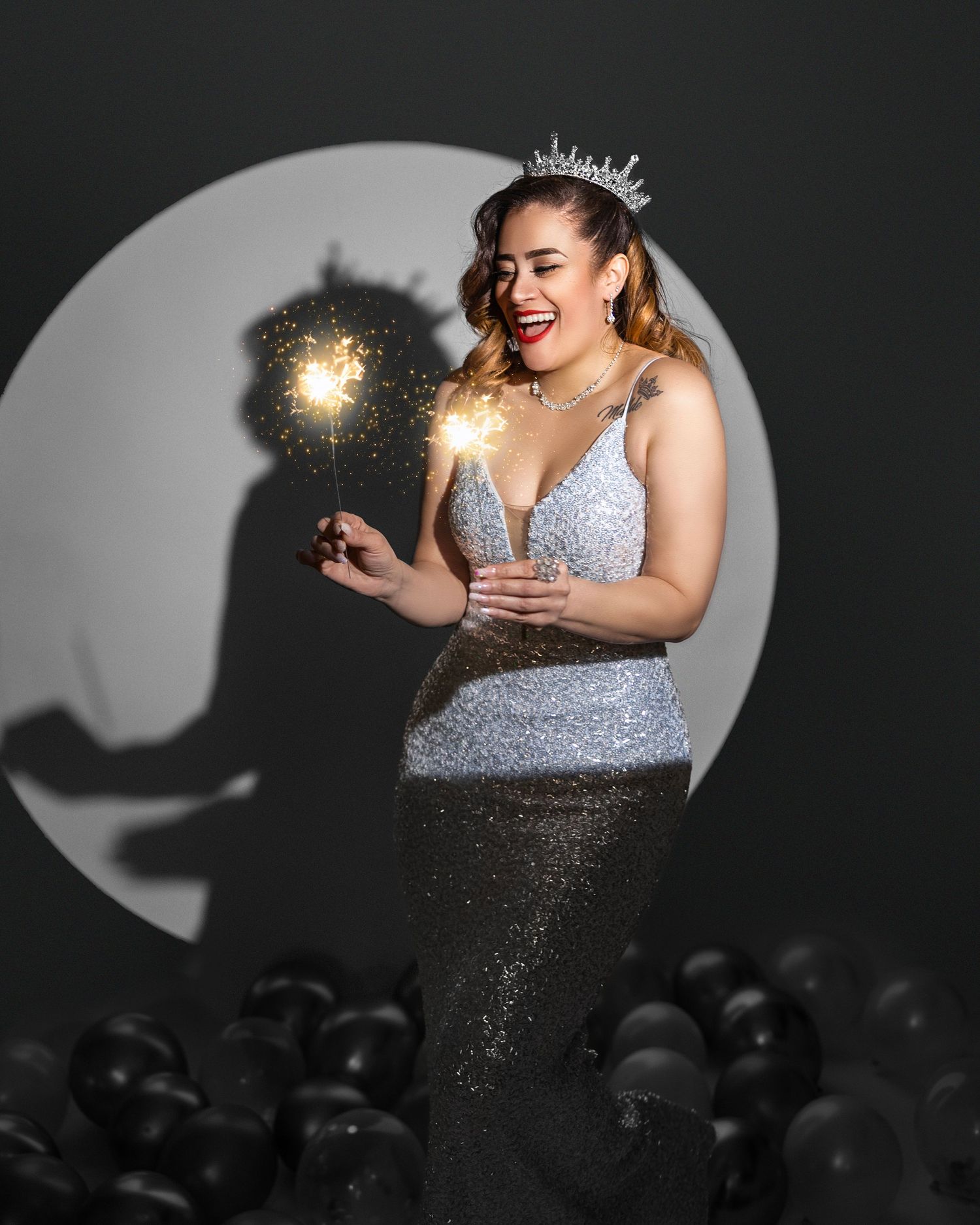 Festive portrait with sparkler and tiara against dark background with balloons.