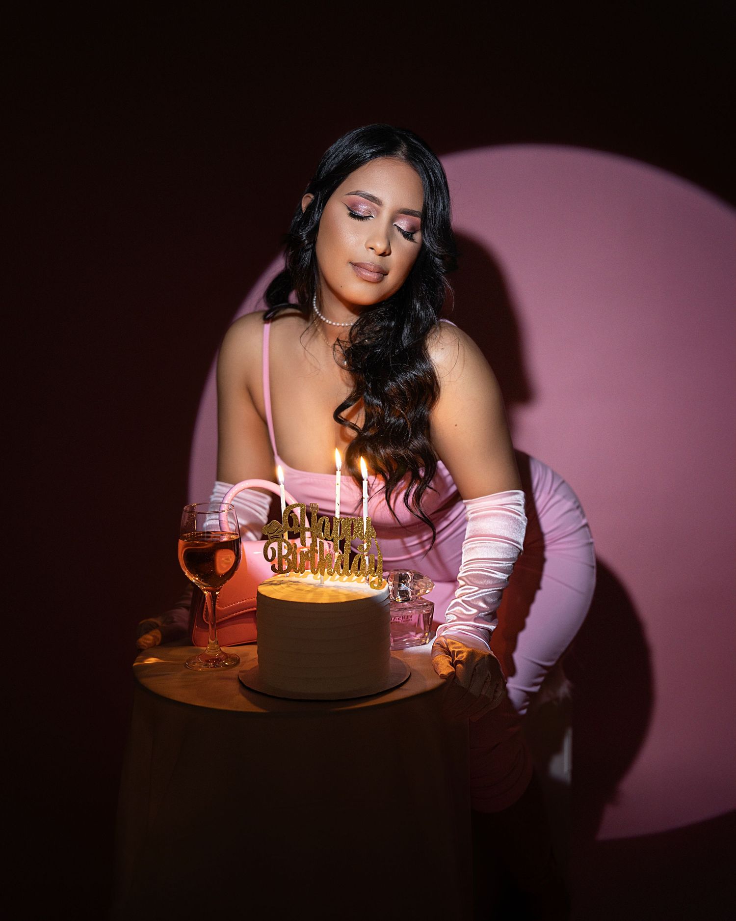 Birthday celebration setup with cake, candles and pink decor in dramatic lighting.