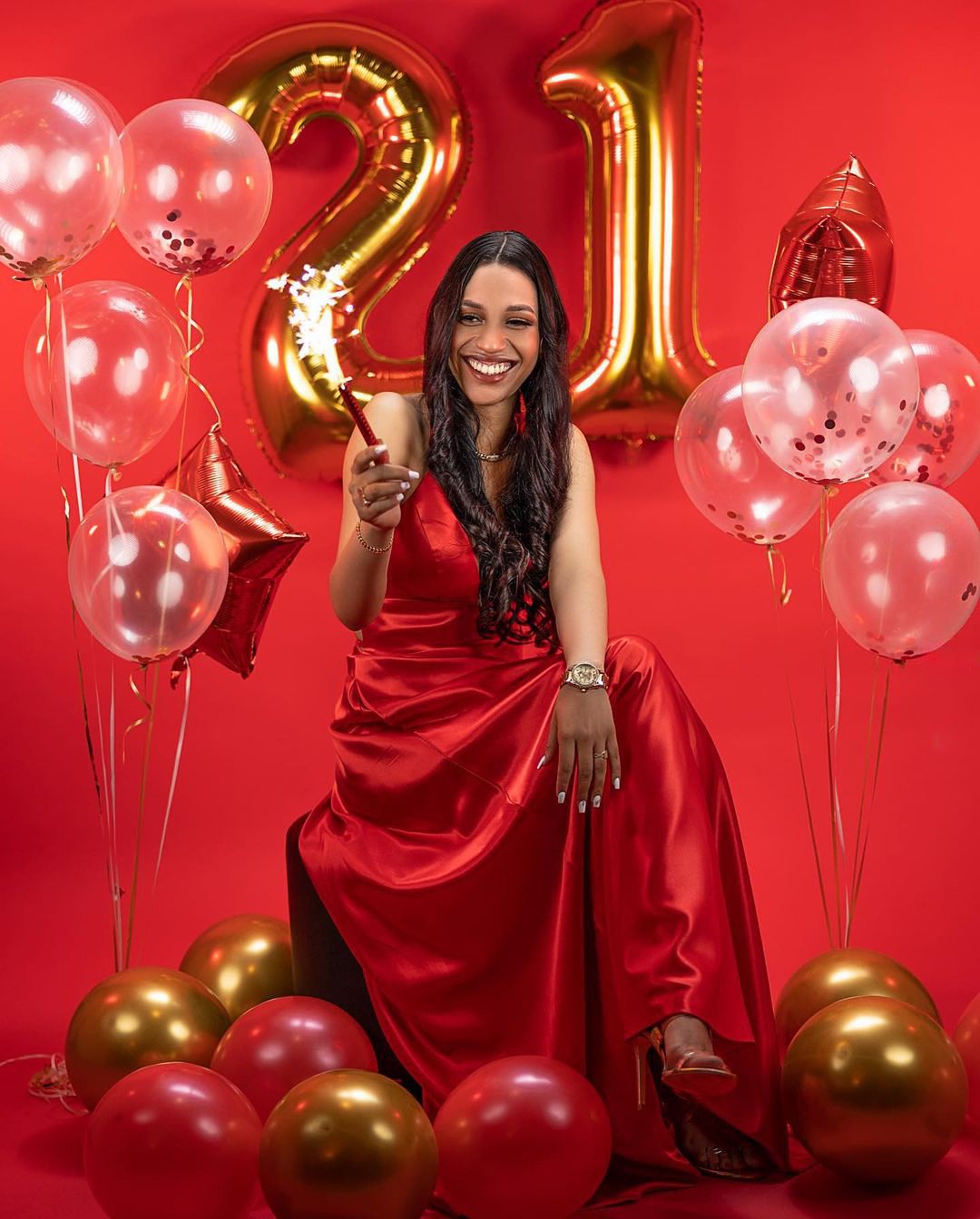 21st birthday celebration with red and gold balloons against red backdrop.