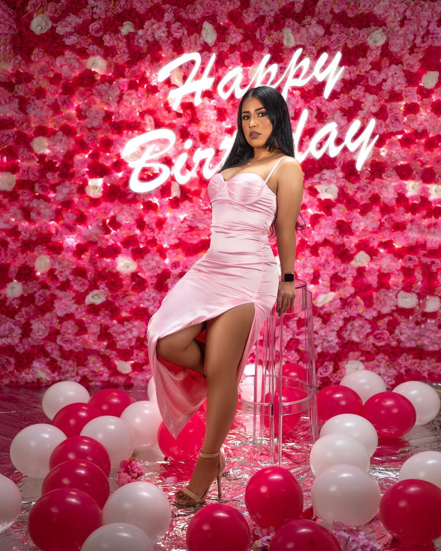 Birthday photoshoot with pink neon sign, floral wall, and red and white balloons.