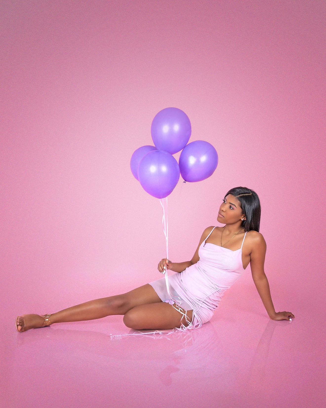 Studio portrait with purple balloons against pink backdrop.